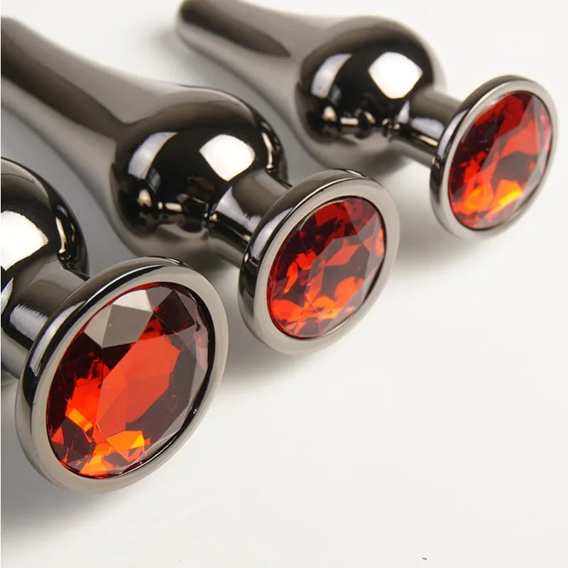 Set of three metal plugs with red gem bases, reflective finish on white background