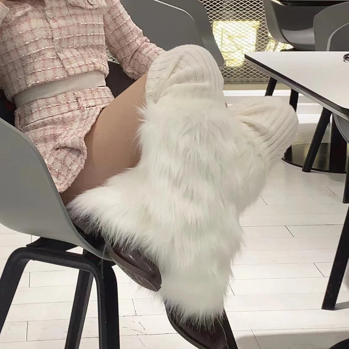 Woman sitting on chair wearing white faux fur knee-high boots and textured pink outfit