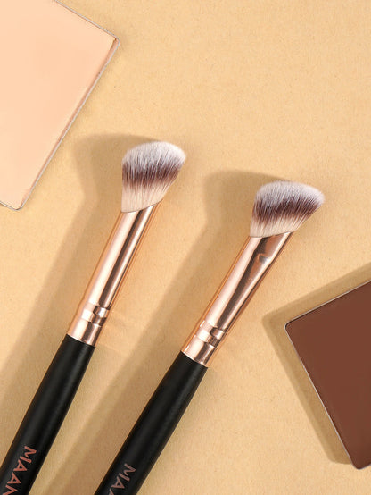 Two angled makeup brushes with black handles and rose gold ferrules on a beige background, surrounded by neutral-toned powder cosmetics.