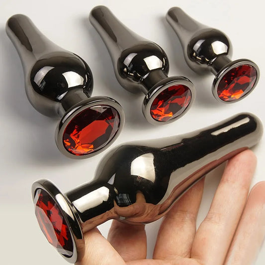 Set of four black metal plugs with red gemstone bases, displayed on a neutral background.