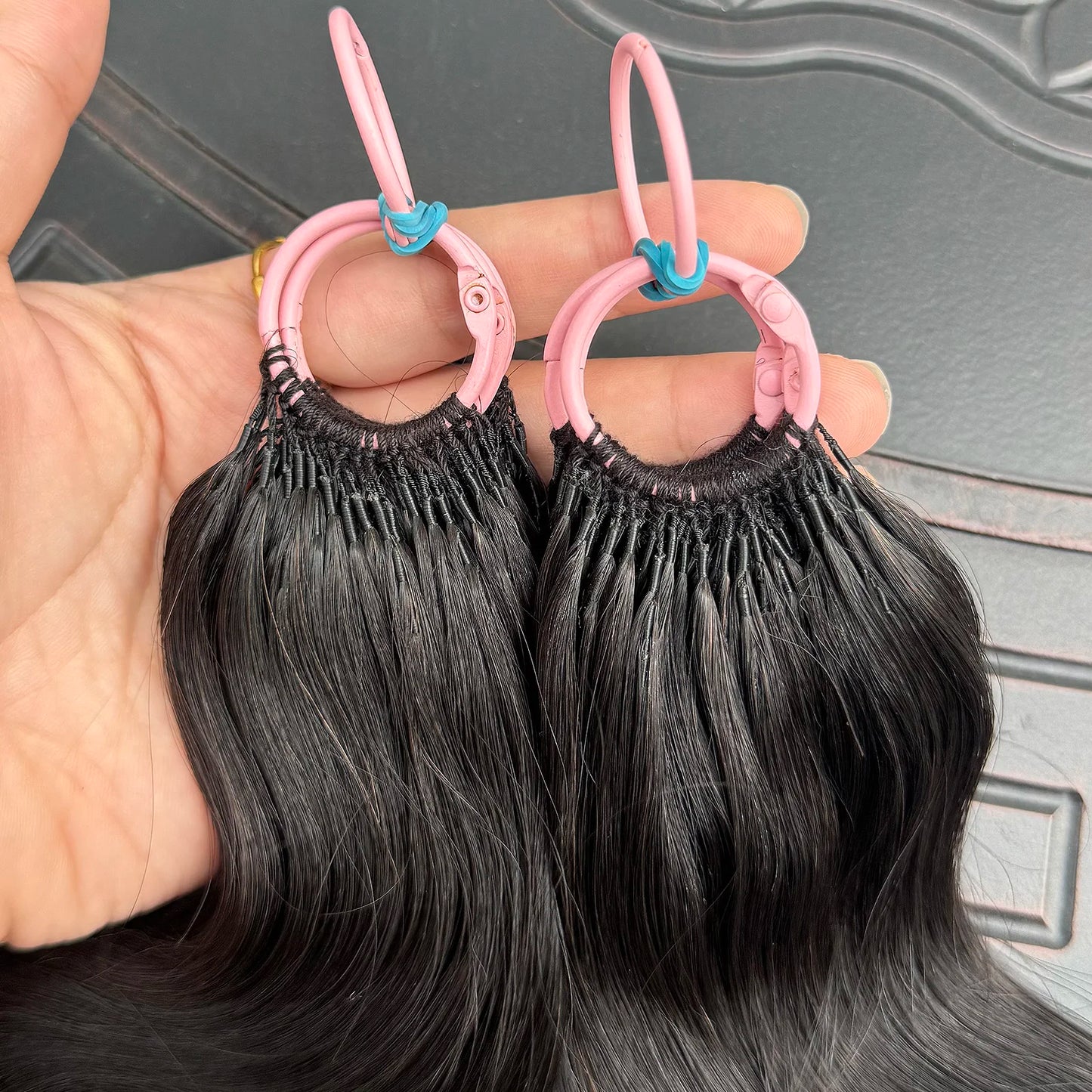 Hand holding black hair extensions attached to pink plastic loops with blue clips