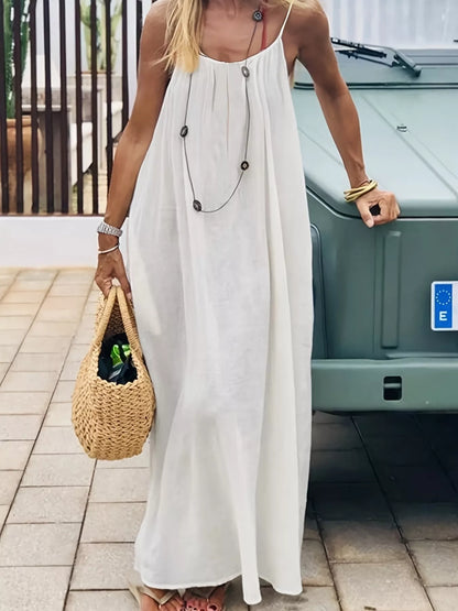 Woman wearing a white maxi dress with spaghetti straps, holding a straw tote bag outdoors